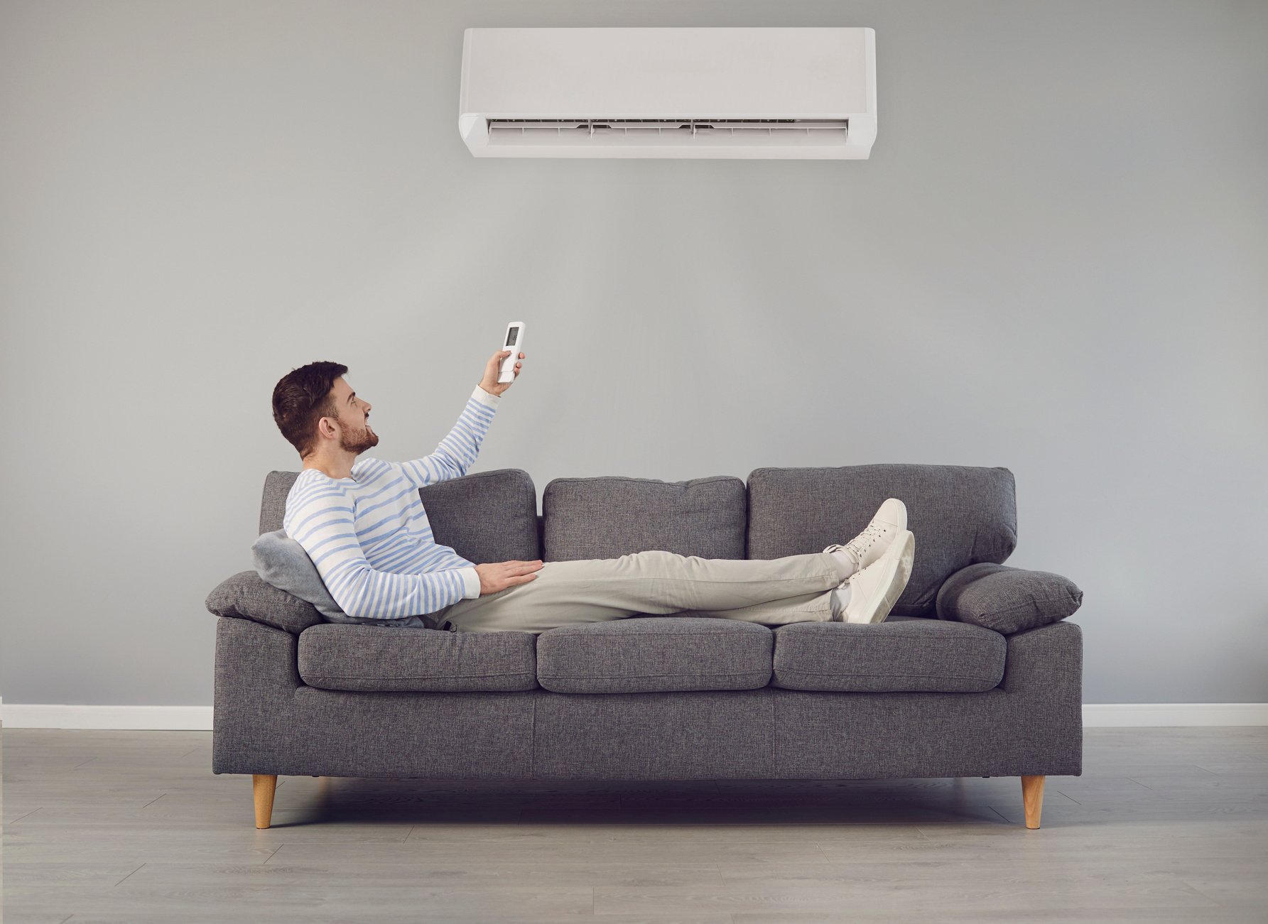 The Young Man Turns on the Air Conditioner Cools the Air While Sitting on the Sofa in the Room